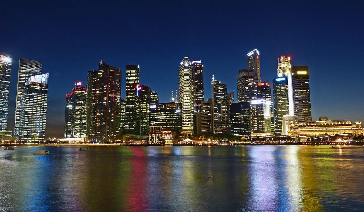 夜晚的城市街景，玻璃幕墙上反射着暖橙色灯光与流动车轨，行人撑伞走过，画面呈现国际无限日话题在城市中悄然扩散的氛围